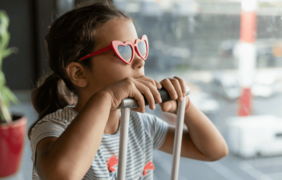 Foto de niña con gafas de sol y manija de maleta de viaje en sus manos a la altura de su menton